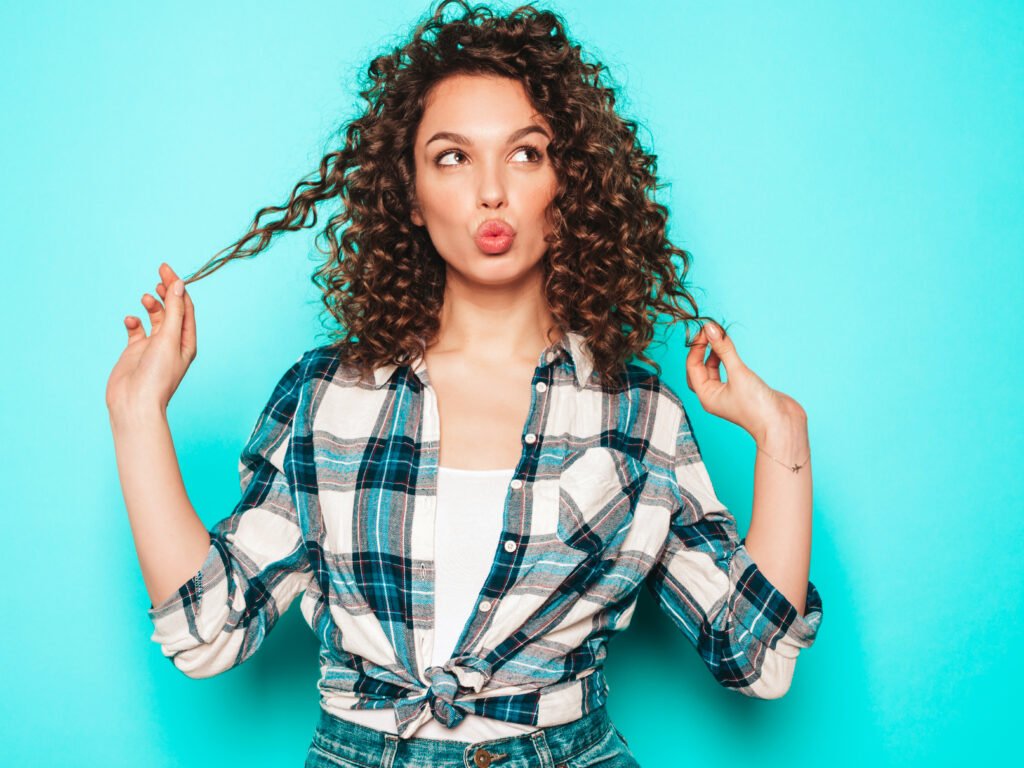 Home portrait of beautiful smiling model with afro curls hairstyle dressed in summer hipster clothes.sexy carefree girl posing in studio near blue wall.trendy funny and positive woman
